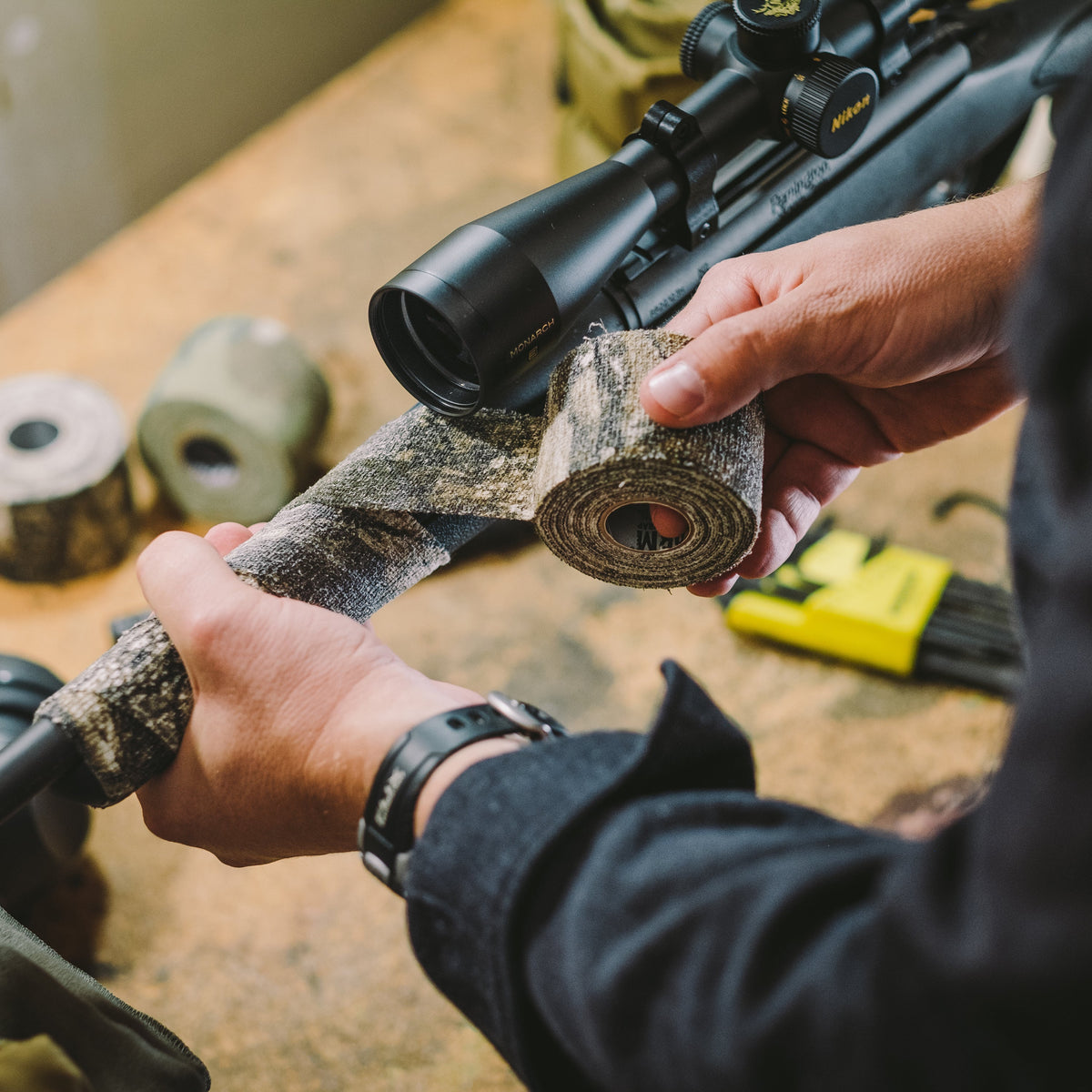 Hands wrapping Camo Form around the fore-end of a rifle below its scope