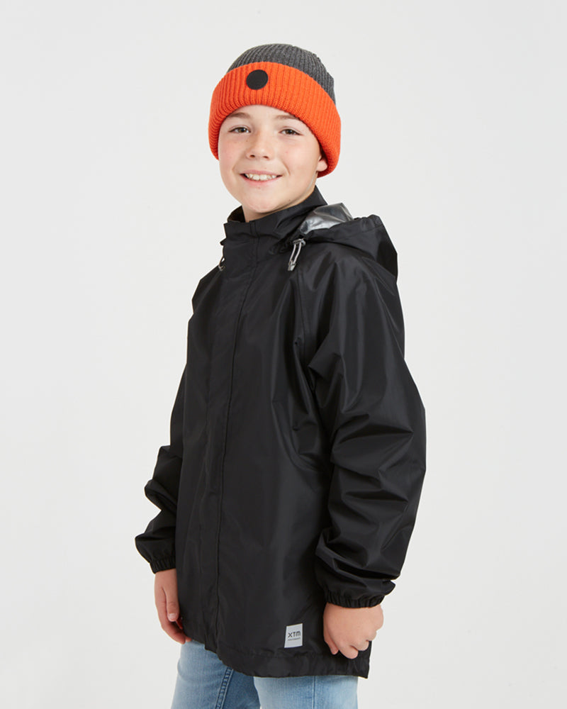 Boy in the XTM Kids Stash 2L rain jacket in Black, angled view showing the side pocket