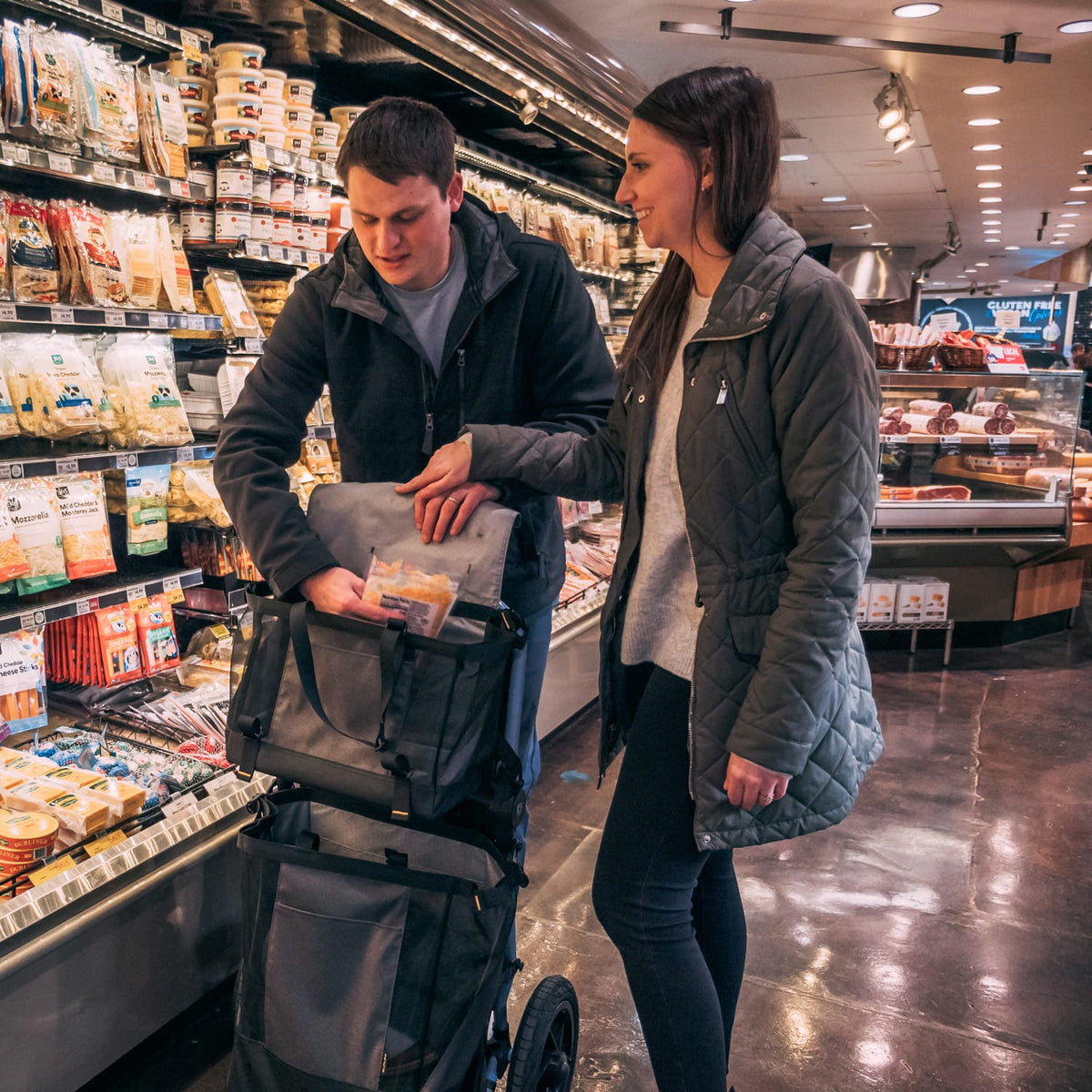 Shopper packing groceries into the Burley Upper Market Bag on a Travoy trailer in a supermarket aisle