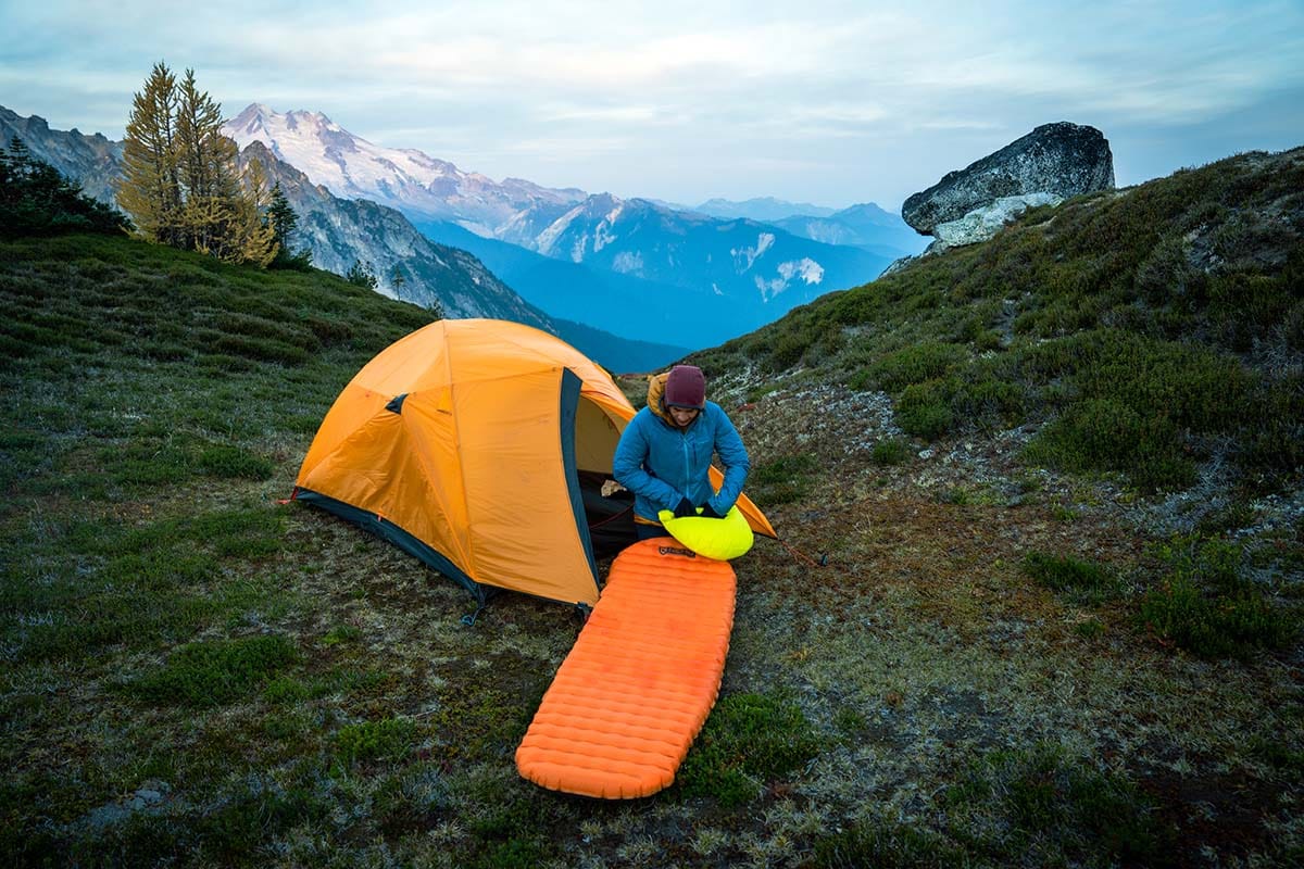 Camper setting up a Nemo sleeping pad outside a tent in an alpine meadow