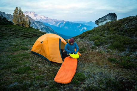 Camper setting up a Nemo sleeping pad outside a tent in an alpine meadow