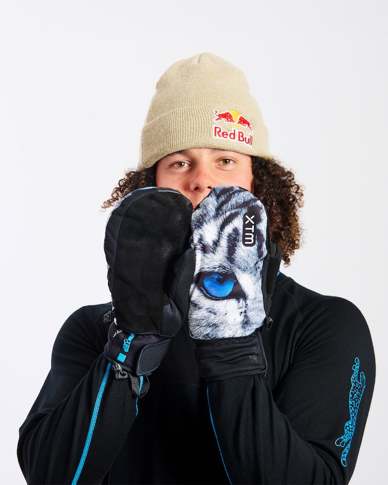Rider holding XTM Snow Leopard mitts to his face, one showing the suede palm and one the print