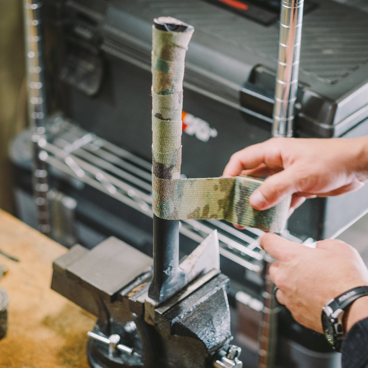 Hands wrapping Camo Form around a metal pole held in a bench vice