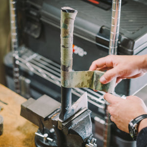 Hands wrapping Camo Form around a metal pole held in a bench vice