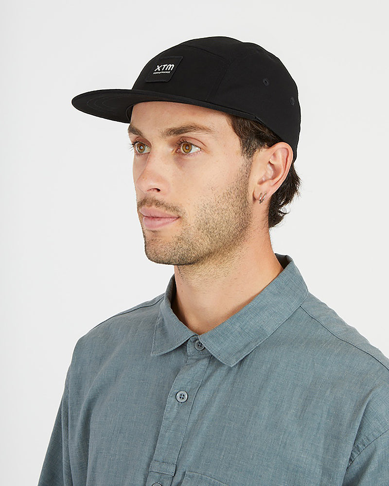 Man wearing the XTM Hakea cap in Black, side view showing the flat peak and logo patch