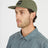 Man in profile wearing the Thyme green XTM Hakea cap with flat peak and square logo patch