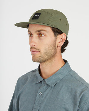 Man in profile wearing the Thyme green XTM Hakea cap with flat peak and square logo patch