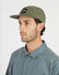 Man in profile wearing the Thyme green XTM Hakea cap with flat peak and square logo patch