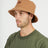 Man wearing the XTM Sundew hemp-cotton bucket hat in Woodsmoke tan, three-quarter view