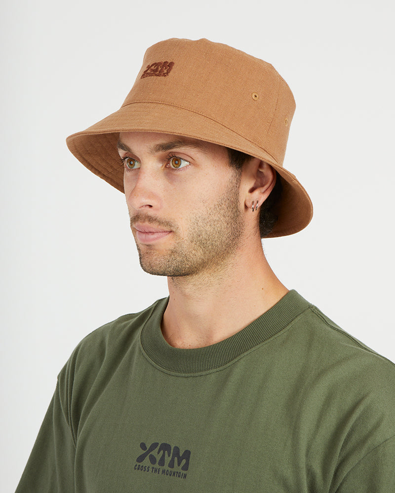 Man wearing the XTM Sundew hemp-cotton bucket hat in Woodsmoke tan, three-quarter view