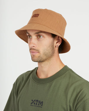 Man wearing the XTM Sundew hemp-cotton bucket hat in Woodsmoke tan, three-quarter view