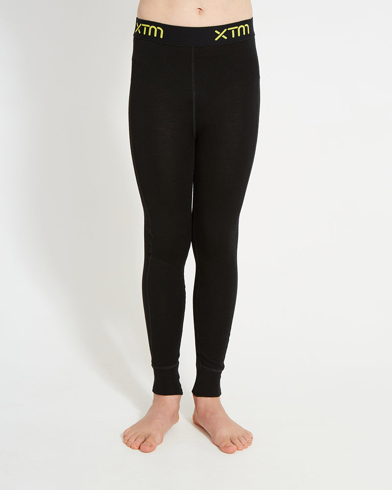 XTM Kids Alpine230 Merino Thermal Pants in Black, front view showing the yellow XTM jacquard waistband
