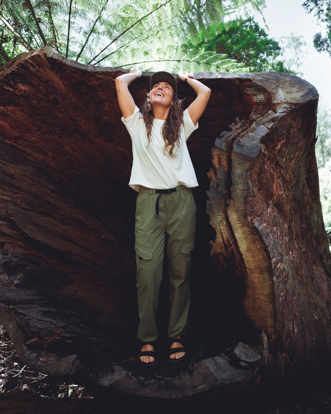 Woman in XTM Acacia Olive hiking pants standing inside a hollow tree trunk in rainforest