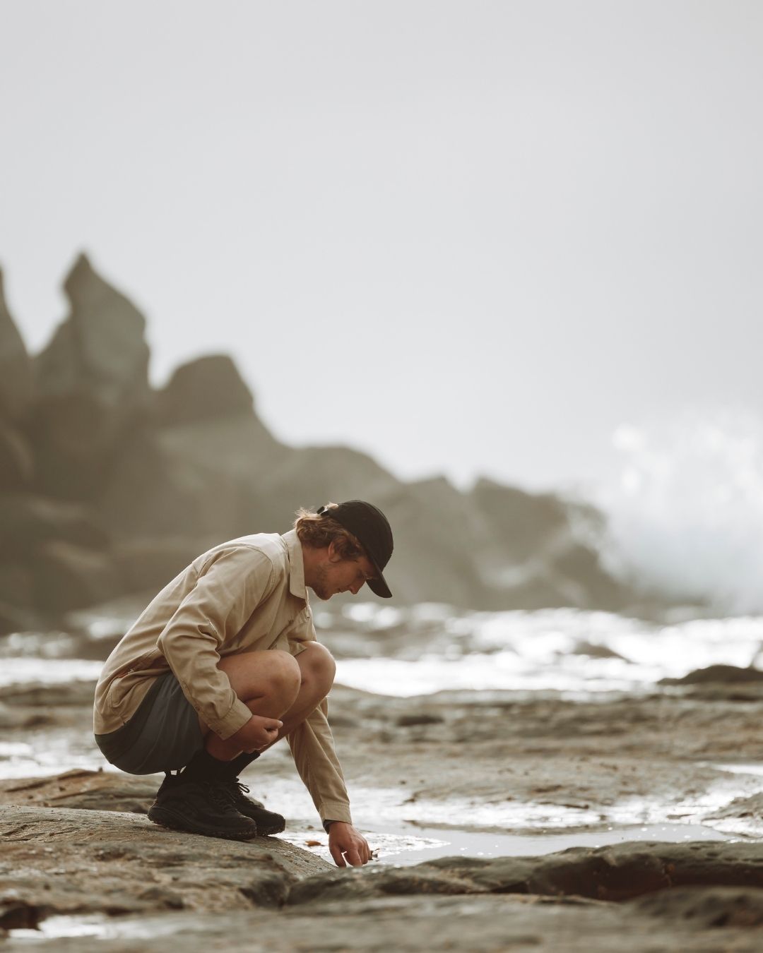 Man crouching on a coastal rock shelf in the Dune XTM Messmate hemp blend shirt