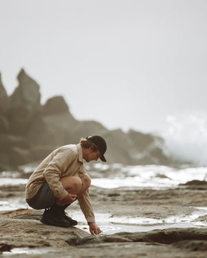 Man crouching on a coastal rock shelf in the Dune XTM Messmate hemp blend shirt