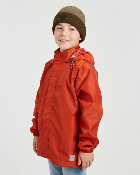 Boy in the XTM Kids Stash 2L packable rain jacket in Burnt Orange, three-quarter front view