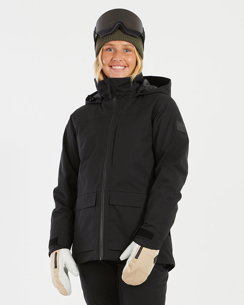 Woman wearing the XTM Elevation II ski jacket in black, front view zipped up with goggles and mittens