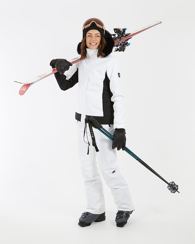 Woman carrying skis and poles in the white XTM Solace women's ski jacket