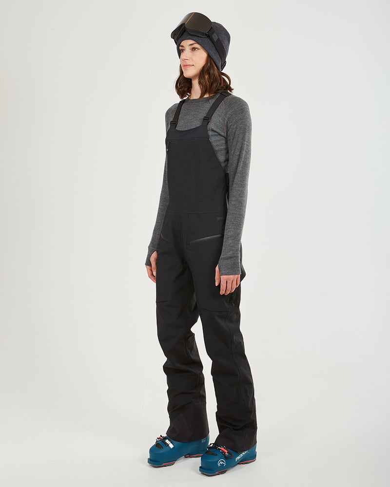 Three-quarter view of the black XTM Stellar 2.0 ski bib pant with ski boots