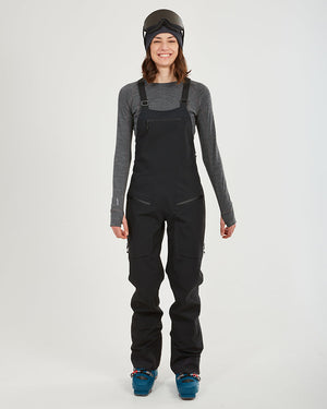 Woman wearing the black XTM Stellar 2.0 hardshell bib pant with ski boots, front view