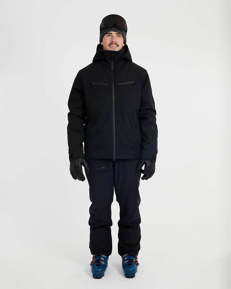 Full-length front view of the Black XTM Quantum snow jacket with black pants and ski boots