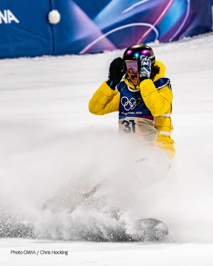 Snowboarder in a yellow jacket sliding to a stop, one XTM Snow Leopard mitt raised to his goggles