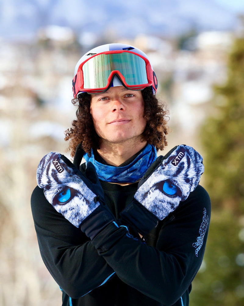 Rider in a helmet and goggles crossing arms in XTM Snow Leopard mitts against a snowy backdrop