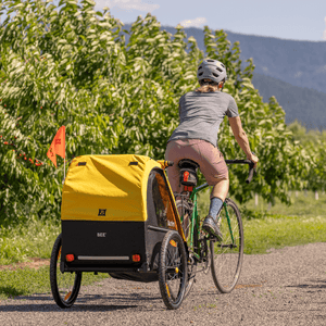 Rider towing a yellow Burley Bee trailer along a gravel path