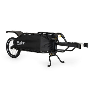 Burley Coho XC single-wheel cargo trailer in black, standing on its kickstand, tow arm to the right