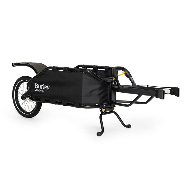 Burley Coho XC single-wheel cargo trailer in black, standing on its kickstand, tow arm to the right