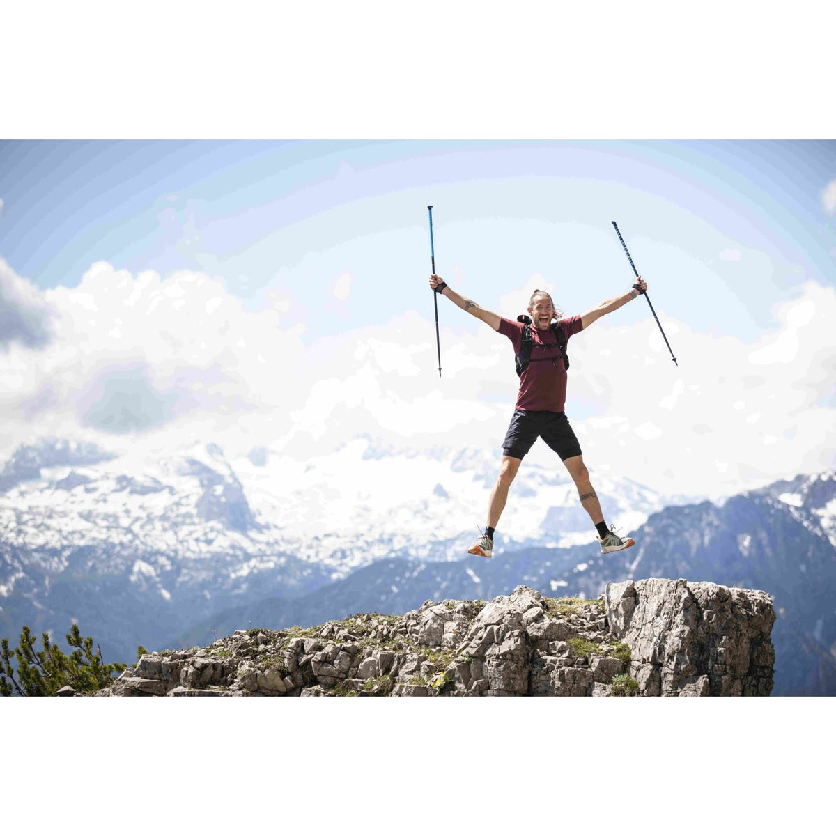 Runner leaping on a rocky mountain summit holding a pair of trail poles