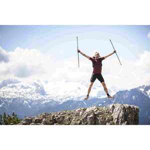 Runner leaping on a rocky mountain summit holding a pair of trail poles
