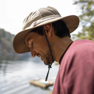 Man wearing a Brushline Bucket hat with the chinstrap down, looking at a lake